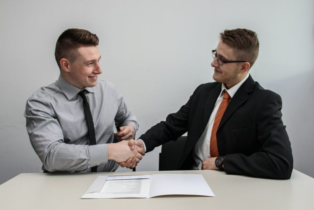 Two men shaking hands over a table with papers.