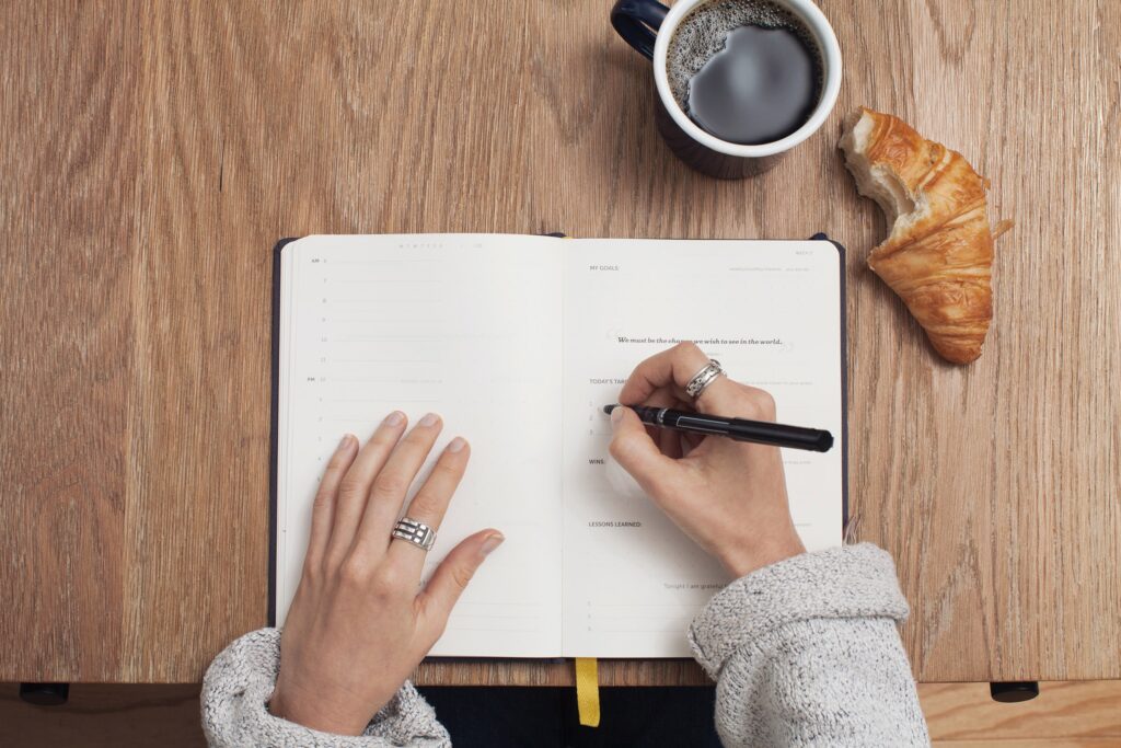 A person writing in a notebook on top of a table.
