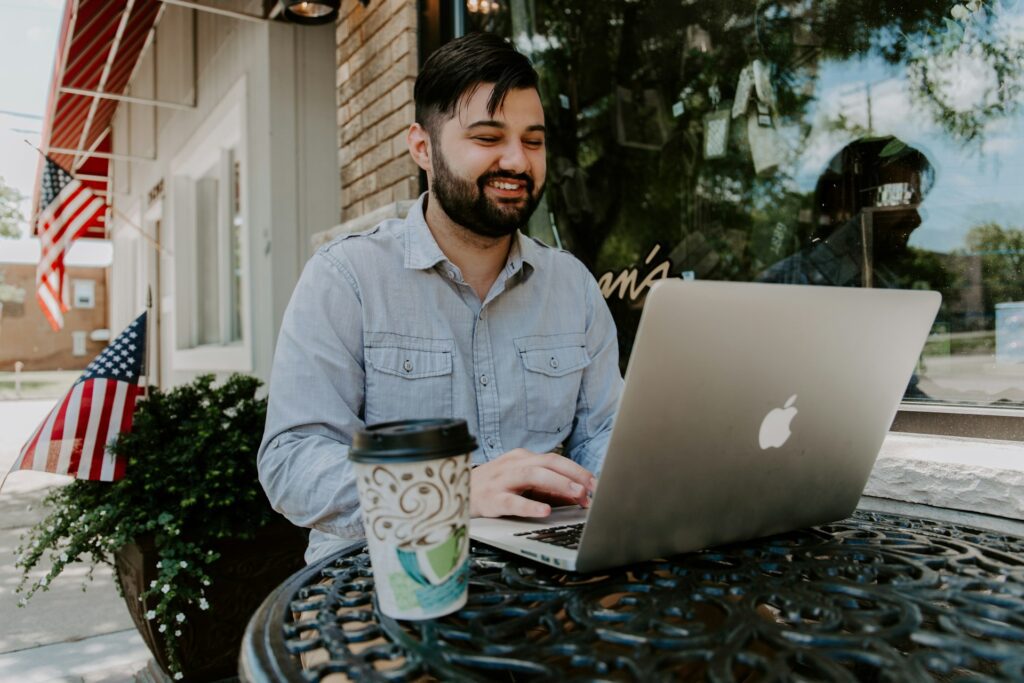A man sitting at an outdoor table with his laptop and coffee.
